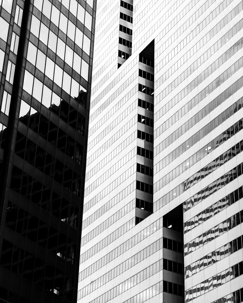 A dark glass facade meets a bright grid of windows in a high-contrast black-and-white architectural study.