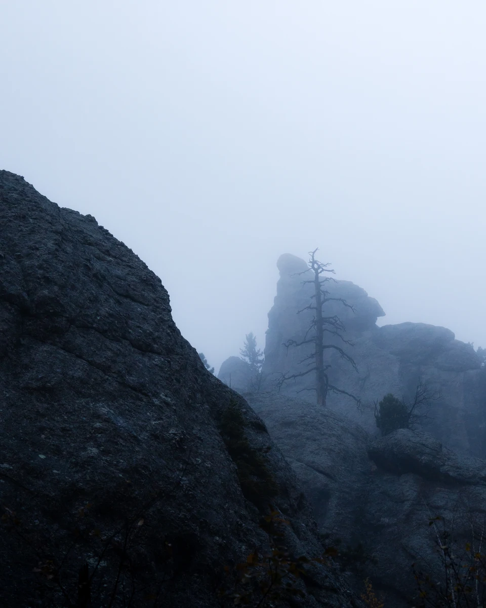 A jagged rock formation emerges through pale blue mist.