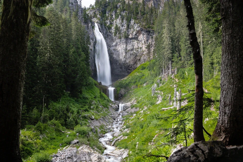 A waterfall descends from a high forested cliff into a rocky valley.