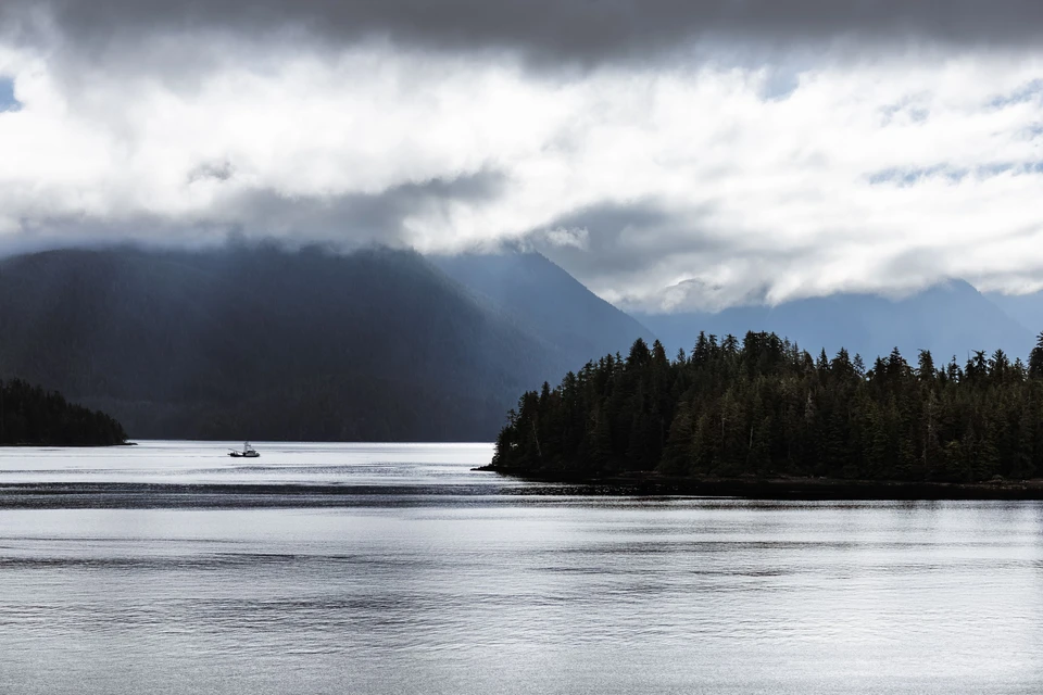 A wooded island and distant mountains beneath a break in the clouds.