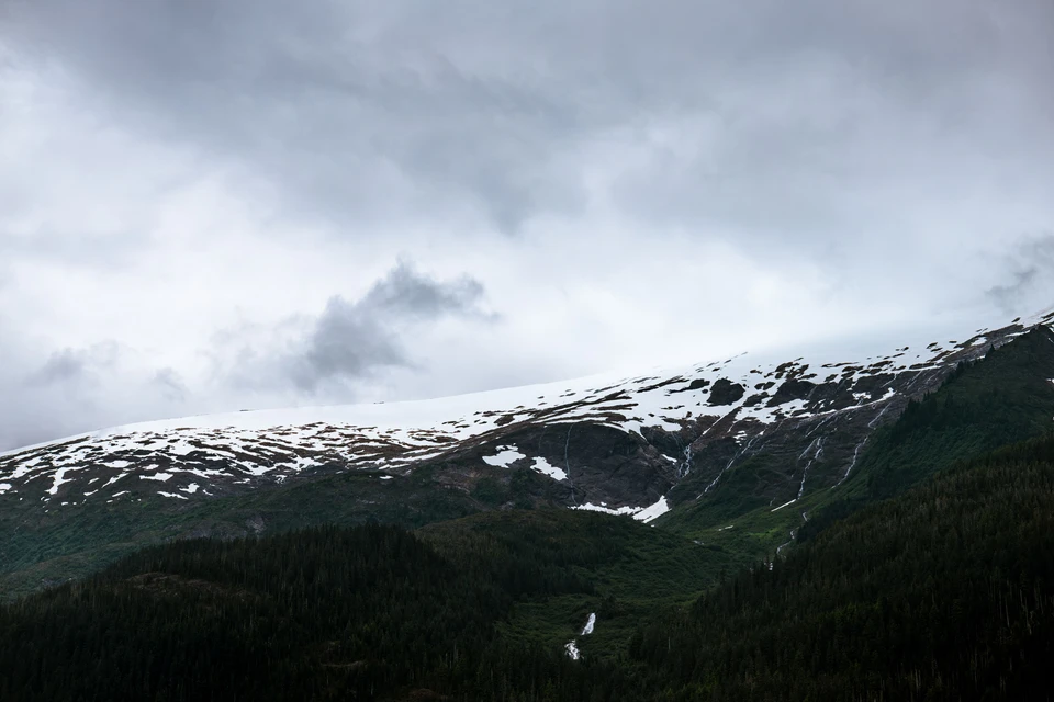 Snow traces a dark mountain ridge under a low, clouded sky.