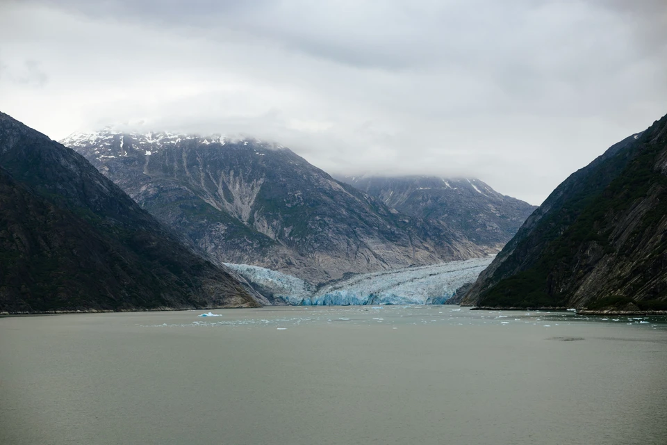 A pale blue glacier rests at the end of a sheltered mountain inlet.