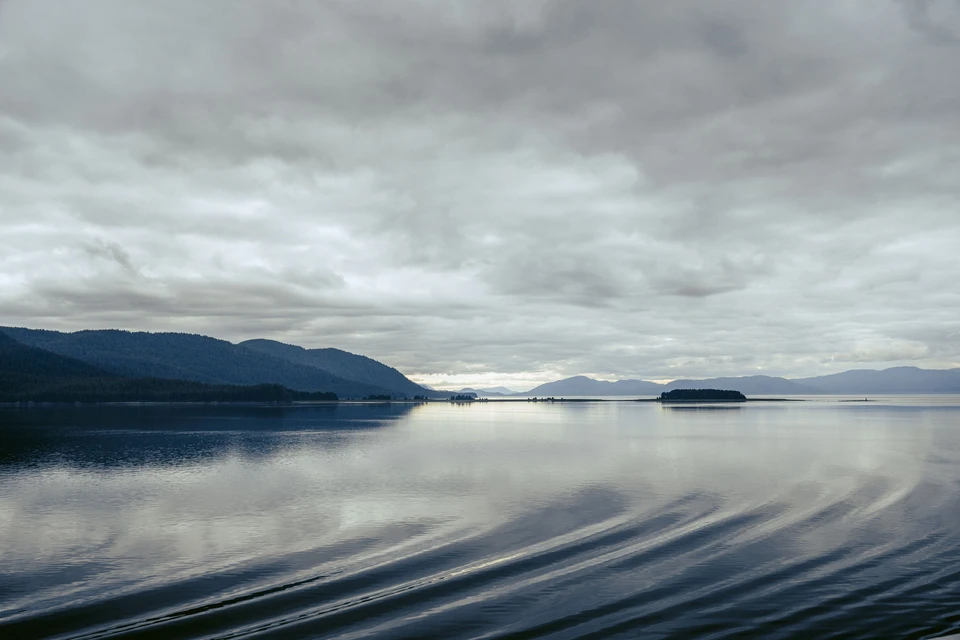 Long curves of reflected clouds cross a still mountain inlet.