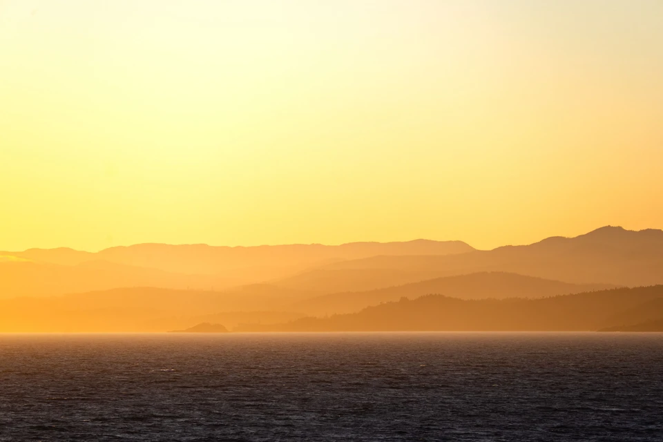 Golden mountain silhouettes recede beyond a dark sea.