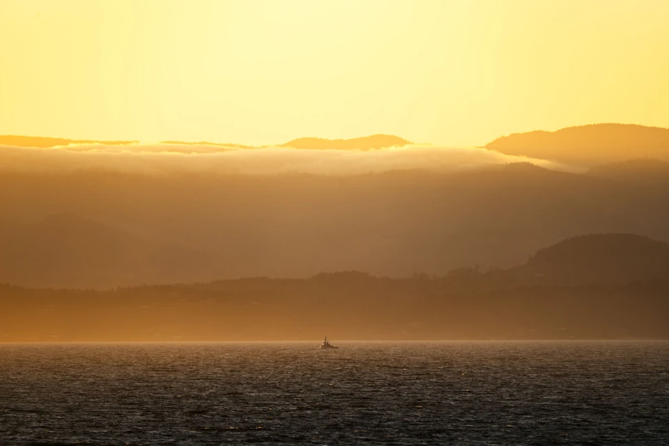 Low clouds drift between warm mountain ridges above the sea.